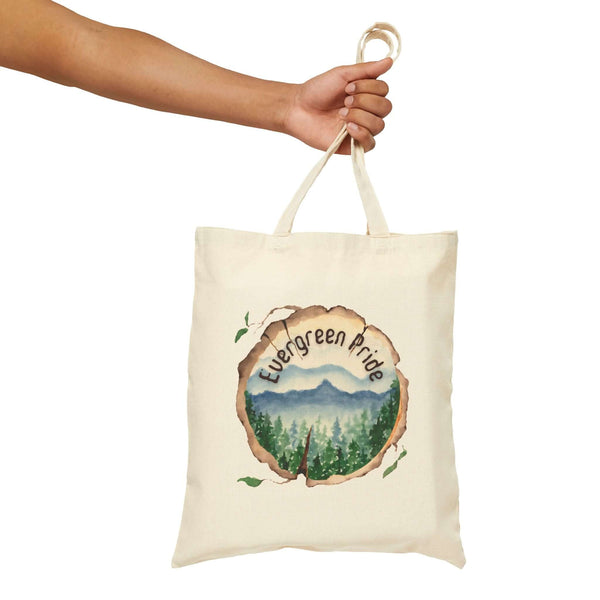 Hand holding Evergreen Pride cotton tote bag with watercolor wood slice design and forest scene.