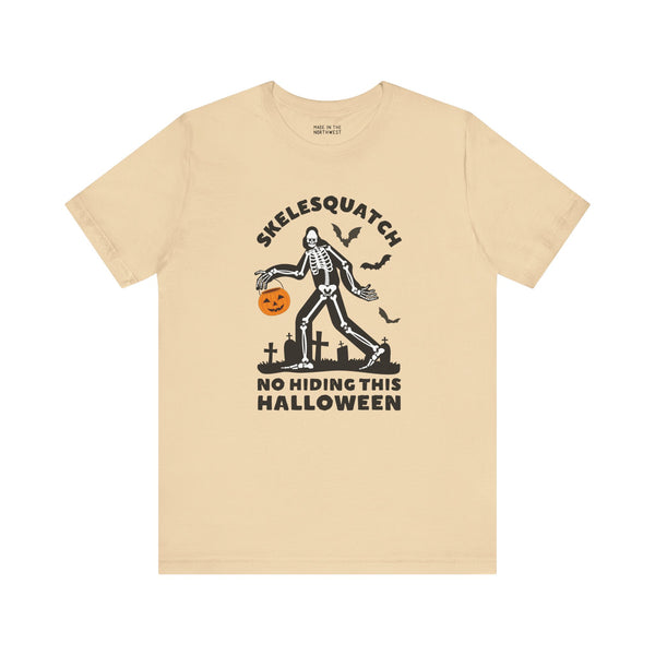 Skelesquatch Halloween premium soft tee featuring a skeleton with a pumpkin, graveyard, and bats design.