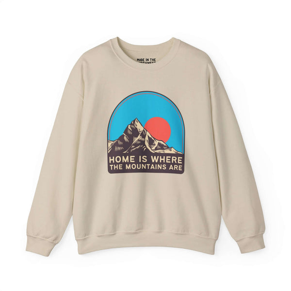 Beige sweatshirt with "Home is Where the Mountains Are" and mountain graphic against a blue and red sky circle design.