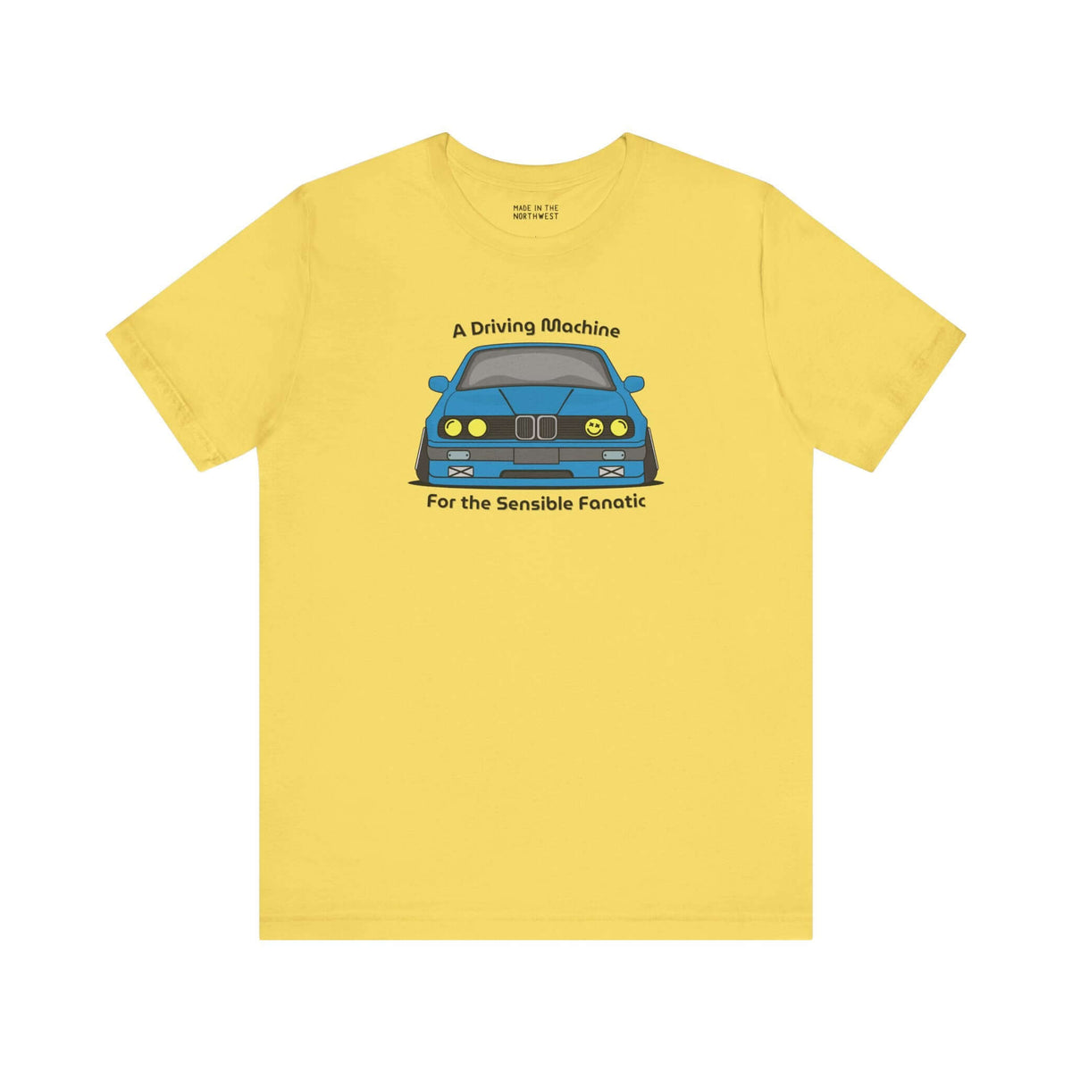 Yellow soft tee featuring the illustration of a BMW E30 with the text 'A Driving Machine for the Sensible Fanatic'.