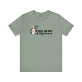 Premium olive green tee featuring 'Plant Seeds of Kindness' design with a peace sign and blooming flowers.