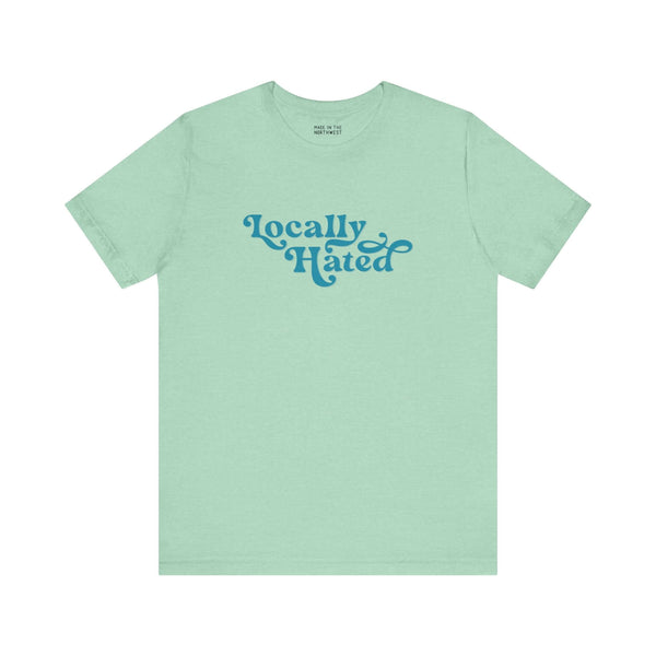 Light green "Locally Hated" soft tee with bold cursive font, designed for those who stand out in the Pacific Northwest.