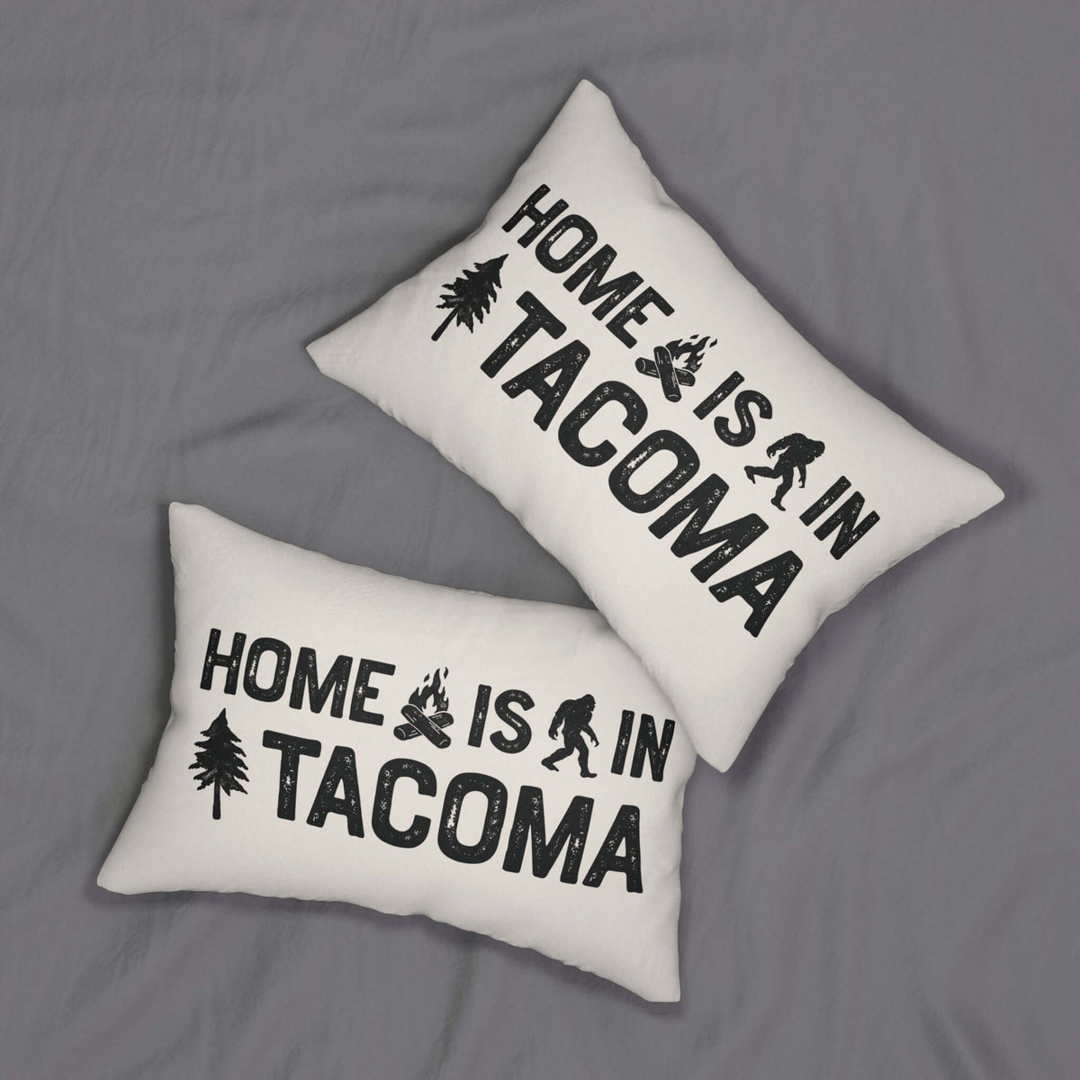 Home is in Tacoma Lumbar Accent Pillow on a gray fabric background, featuring bold text and campfire graphics.