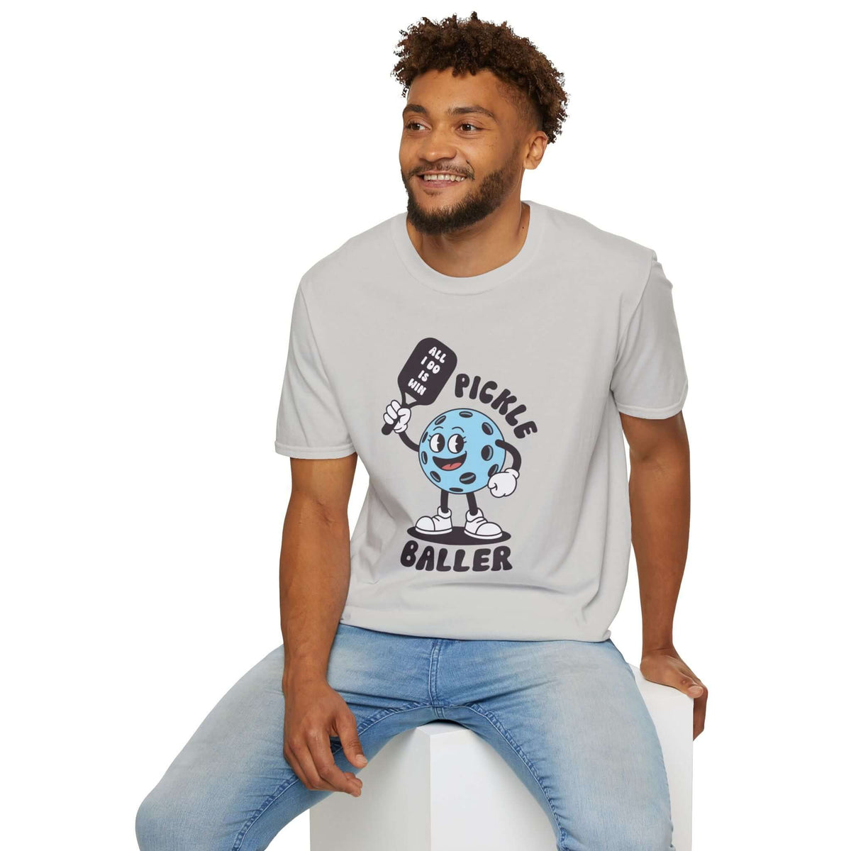 Man wearing a light gray Pickle Baller T Shirt featuring a playful pickleball character.