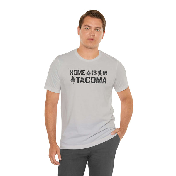 Home is in Tacoma tee worn by a man, showcasing Tacoma's pride with campfire and tree designs.