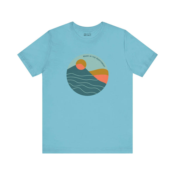 Pacific Peaks Modern Circle Soft Tee in blue with a graphic of a mountain scene and sunset, inspired by the Pacific Northwest.