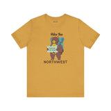 Hike the Northwest t shirt featuring a playful bear with a backpack and map in a soft yellow color.