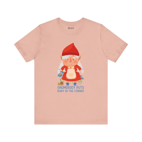 Light pink t-shirt featuring a playful gnome and the phrase 'Gnomebody Puts Baby in the Corner' for fun wardrobe flair.