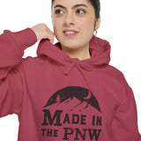 Woman wearing a cozy Made in the PNW hoodie, showing outdoor style and Northwest pride with a mountain and forest design.
