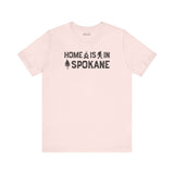 Home Is in Spokane Tee featuring campfire, Bigfoot, and tree illustrations representing Spokane pride.