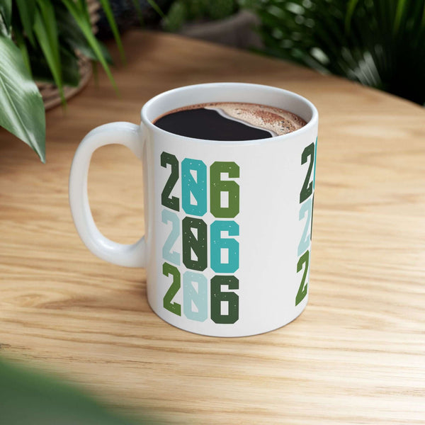 Two-Oh-Six Pop Seattle ceramic mug with bold 206 design resting on wooden table surrounded by greenery.