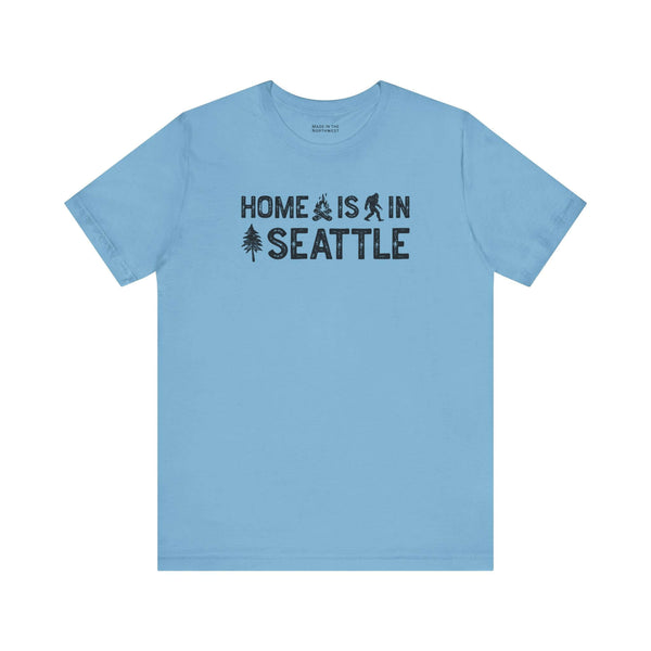 Home Is in Seattle Tee in blue with campfire, Bigfoot, and tree design, representing Emerald City pride.