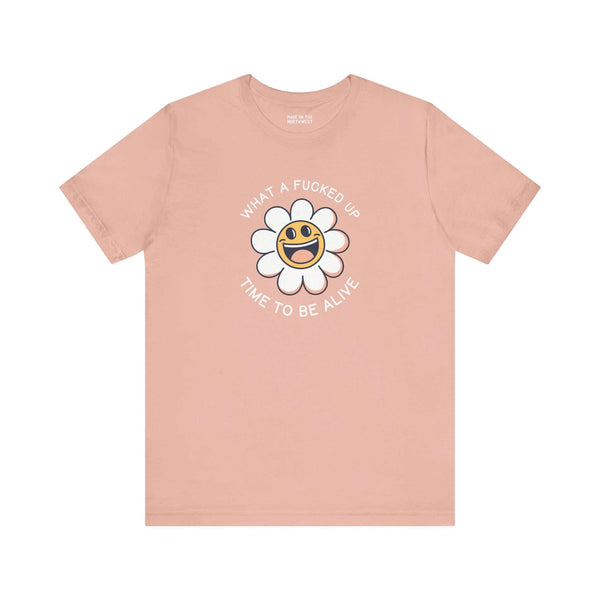 Pink premium tee with smiling daisy graphic and text "What a F*cked Up Time to Be Alive" for humorous expression.