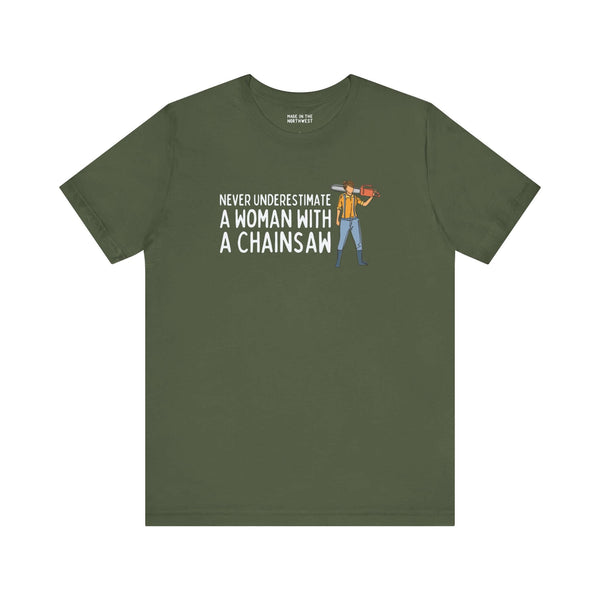 Olive green tee featuring the phrase 'Never Underestimate a Woman with a Chainsaw' and an illustration of a woman with a chainsaw.