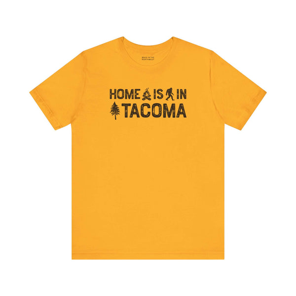Home is in Tacoma tee featuring campfire, Bigfoot, and tree graphics on a yellow shirt.
