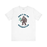 Don’t Be an Assquatch Tee featuring a friendly Bigfoot holding flowers on a white shirt.