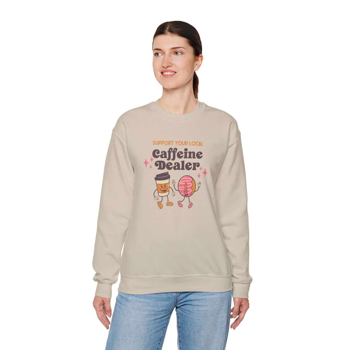 Woman wearing beige Support Your Local Caffeine Dealer sweatshirt featuring playful coffee-themed design.