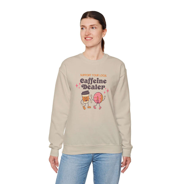 Woman wearing beige Support Your Local Caffeine Dealer sweatshirt featuring playful coffee-themed design.
