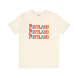 Bold Portland Trio Soft Tee with colorful block-letter design, celebrating Rose City style on a cream background.