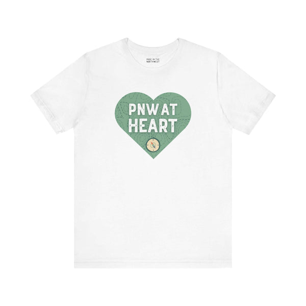 White t-shirt with green heart design featuring "PNW at Heart" text and a compass graphic, representing Pacific Northwest pride.