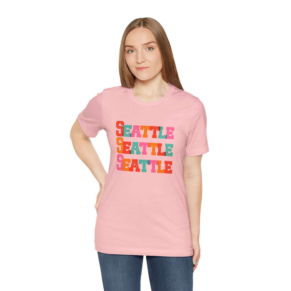 Woman wearing pink Seattle T-shirt with colorful block-letter design, perfect for fans of the Emerald City.