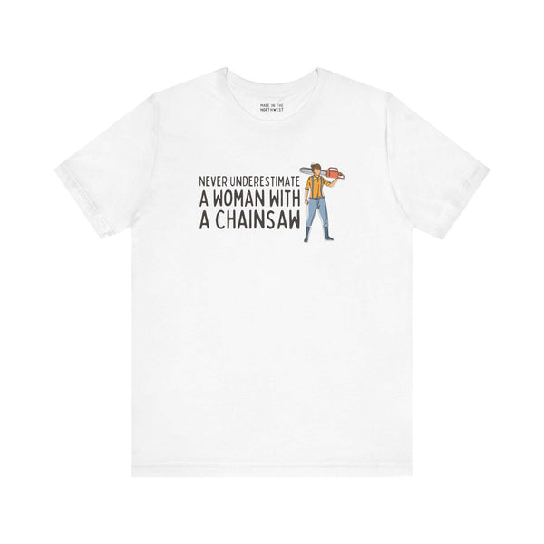 White premium soft tee featuring the quote 'Never Underestimate a Woman with a Chainsaw' and an illustration of a woman with a chainsaw.