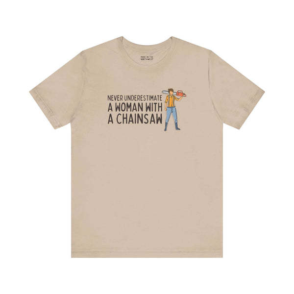 Beige premium soft tee featuring the phrase 'Never Underestimate a Woman with a Chainsaw' and an illustrated figure.
