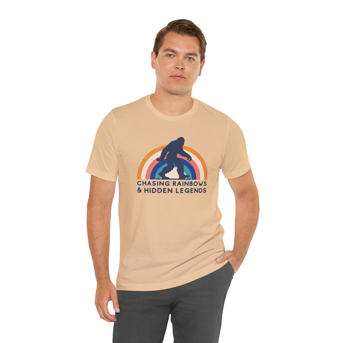 Man wearing Chasing Rainbows and Sasquatch Premium Soft Tee with colorful graphic on a beige shirt.