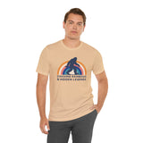 Man wearing Chasing Rainbows and Sasquatch Premium Soft Tee with colorful graphic on a beige shirt.