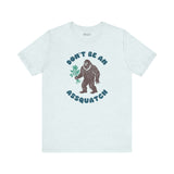 Don't Be an Assquatch Tee featuring a friendly Bigfoot holding flowers in a humorous design.
