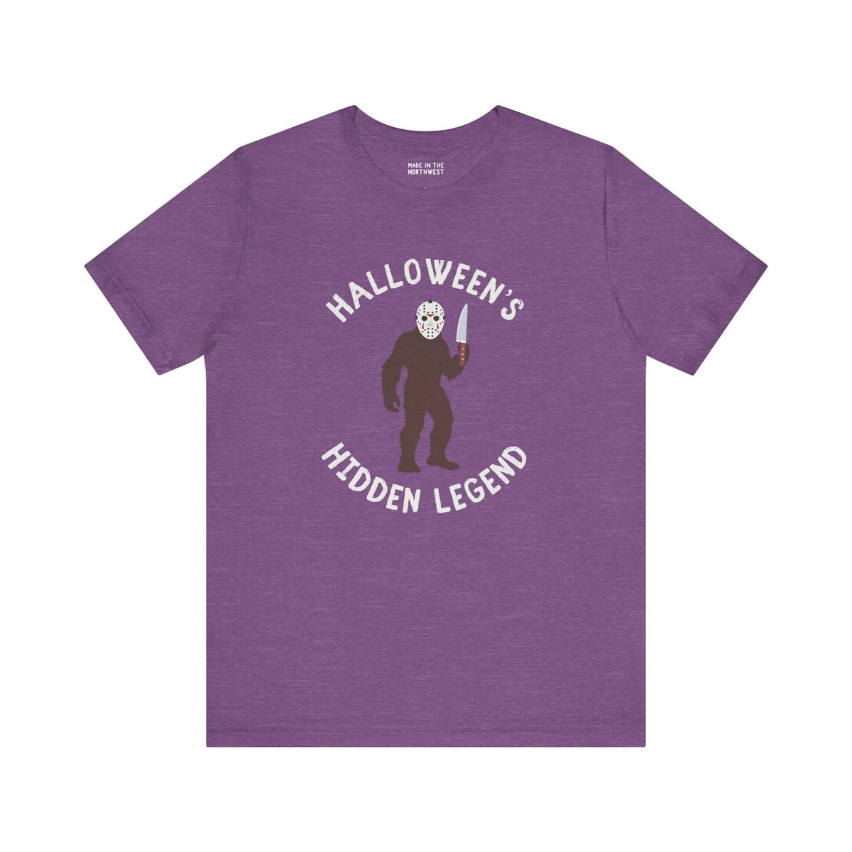Halloween's Hidden Legend Bigfoot tee features a creature in a mask holding a knife on purple fabric.