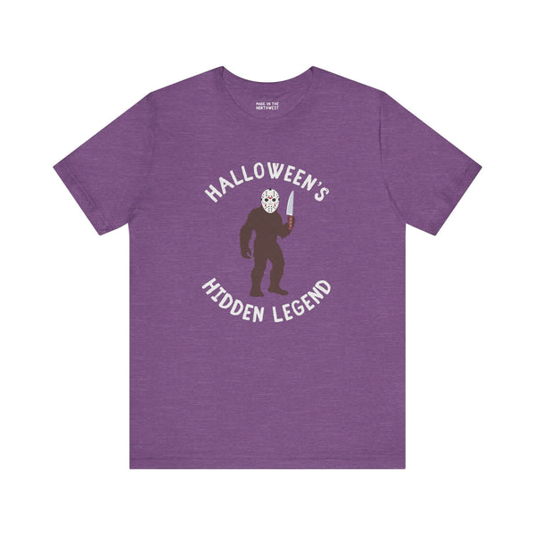 Halloween's Hidden Legend Bigfoot tee features a creature in a mask holding a knife on purple fabric.