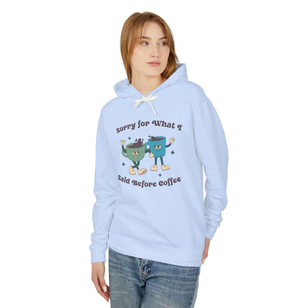 Light blue hoodie with playful text 'Sorry for What I Said Before Coffee' and cartoon coffee cups design.