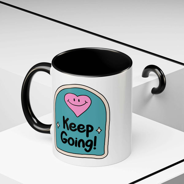 Keep Going Mug featuring a smiling pink heart and hand-lettered message on a teal background.