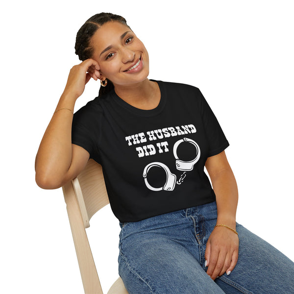 The Husband Did It T Shirt displayed on a smiling woman sitting on a chair, featuring a handcuff graphic.