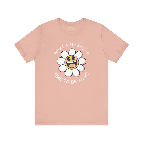 What a F*cked Up Time to Be Alive premium soft tee with smiling daisy design on peach background.
