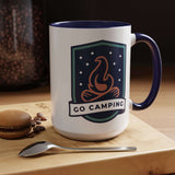 Go Camping Coffee Mug with campfire design and colorful handle on a wooden table with macaron and spoon.