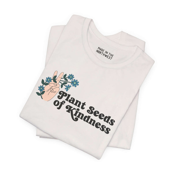 Plant Seeds of Kindness Premium Soft Tee featuring a peace sign hand and blooming flowers on a white shirt.