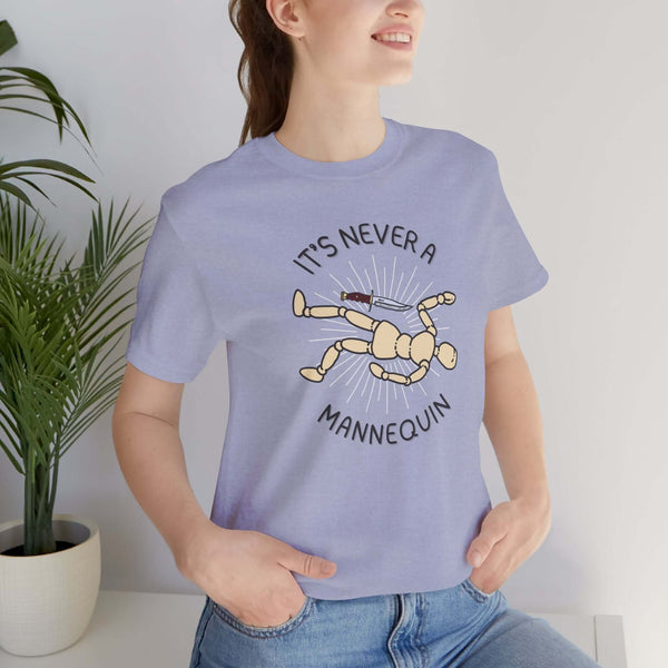 A woman wearing a light blue tee featuring the phrase 'It's Never a Mannequin' with a graphic of a posed mannequin.
