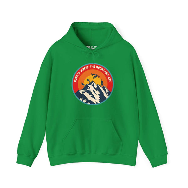 Green hoodie with "Home is Where the Mountains Are" design featuring hiking, motocross, and Bigfoot, inspired by the Pacific Northwest.