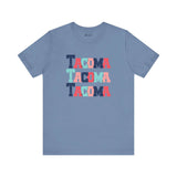 Bold and vibrant Tacoma Trio soft tee featuring colorful block-letter city name on a blue background. Perfect for Tacoma fans.