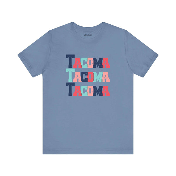 Bold and vibrant Tacoma Trio soft tee featuring colorful block-letter city name on a blue background. Perfect for Tacoma fans.