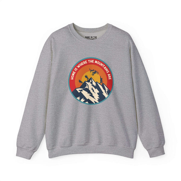 Gray sweatshirt with "Home is Where the Mountains Are" design featuring mountains, motocross, and Bigfoot, celebrating PNW adventure.