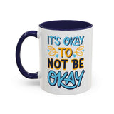 Ceramic mug featuring the phrase 'It's Okay To Not Be Okay' with a colorful design and contrasting blue handle.