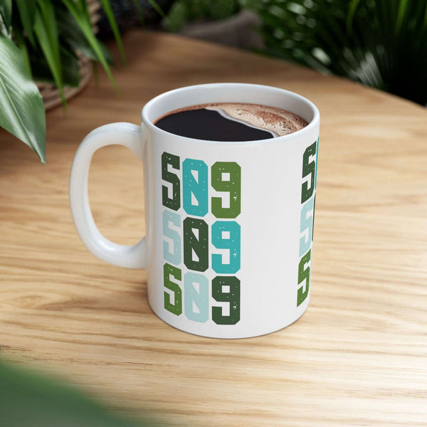 Five-Oh-Nine Pop Spokane ceramic mug with colorful 509 design on wooden surface, perfect for morning coffee.