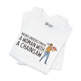 Close-up of a white tee with the phrase 'Never Underestimate a Woman with a Chainsaw' and graphic design.