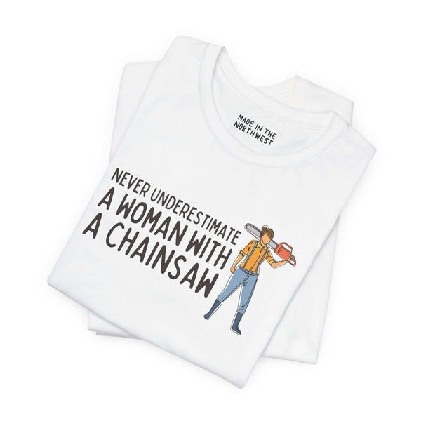 Close-up of a white tee with the phrase 'Never Underestimate a Woman with a Chainsaw' and graphic design.