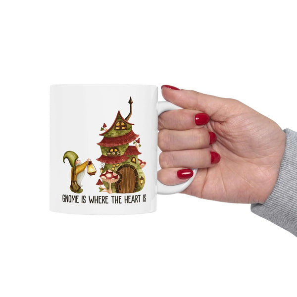 Hand holding a whimsical ceramic mug featuring a gnome and a cozy mushroom house design.