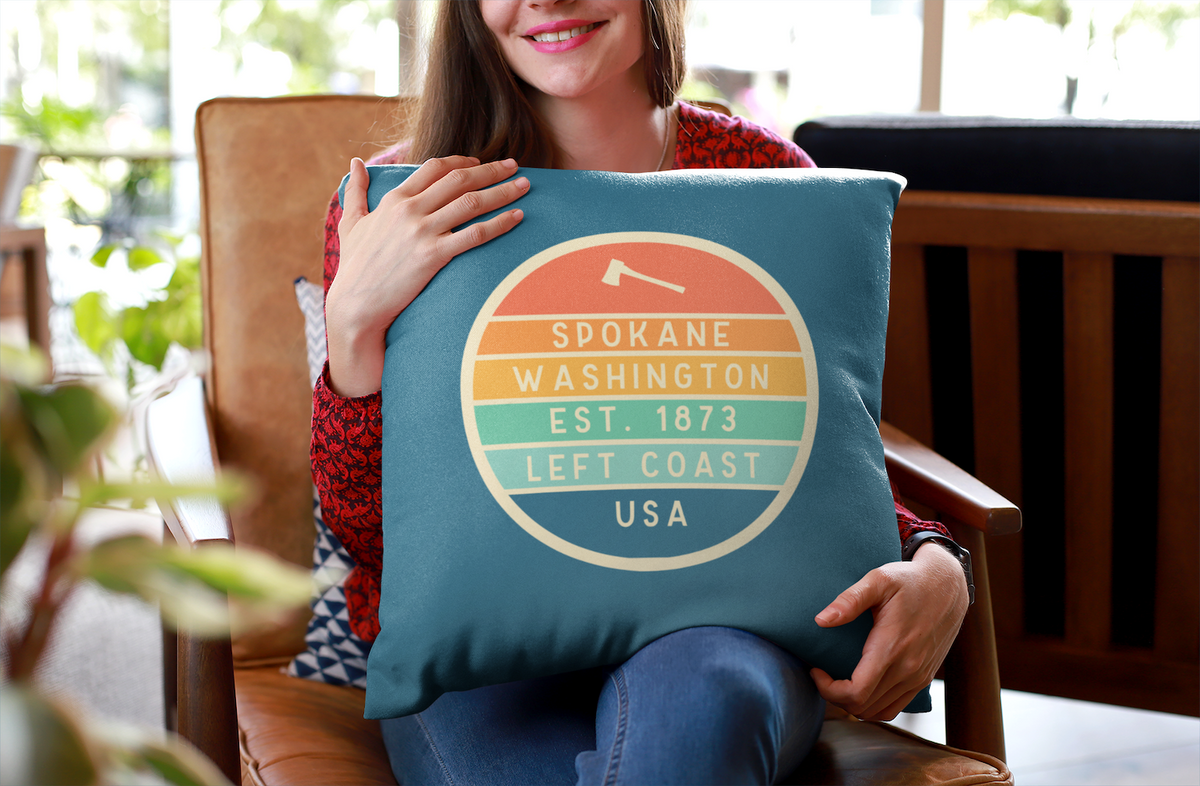 Left Coast Retro Spokane Washington Square Accent Pillow held by a woman in a cozy chair, showcasing its vibrant design.