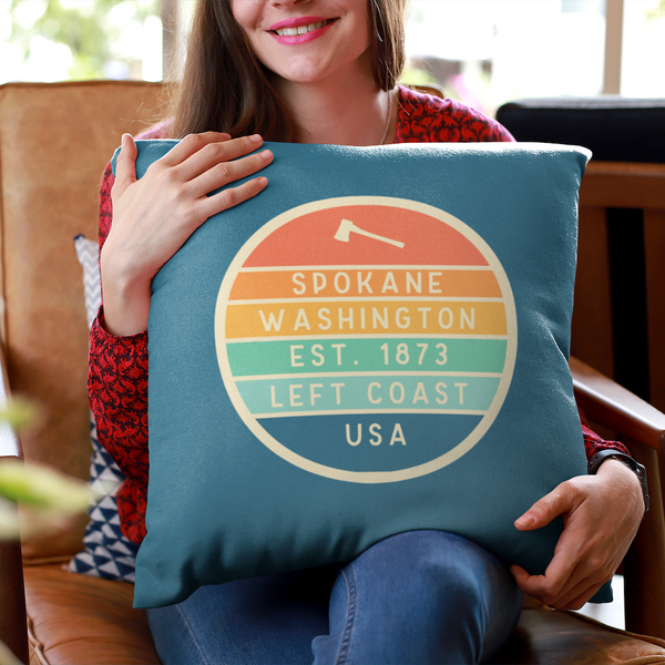 Left Coast Retro Spokane Washington Square Accent Pillow held by a woman in a cozy chair, showcasing its vibrant design.